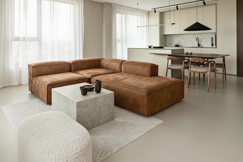 Modernt vardagsrum med en skinsoffa och ljus matta med öppen planlösning mot kök i bakgrunden